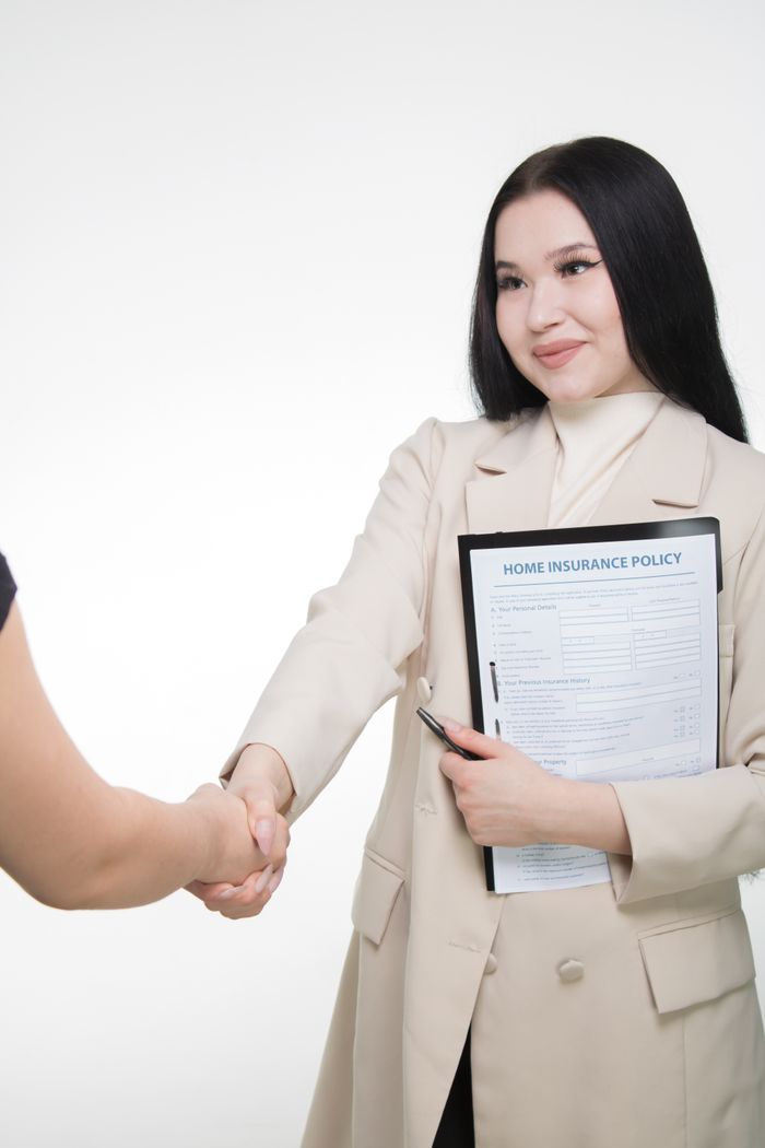 who-we-are Asian woman in office attire shaking hands, holding home insurance policy document.