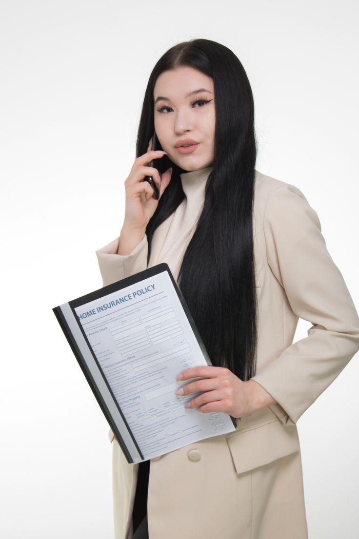 team-01 Confident woman in beige blazer holding a home insurance policy.